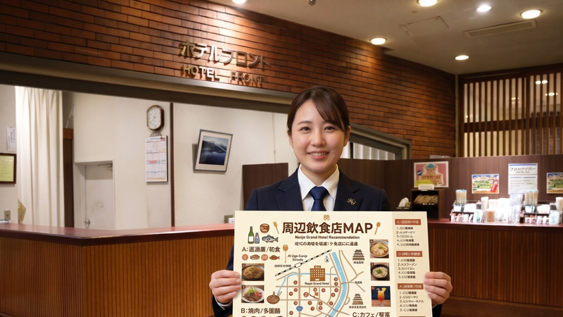 本荘グランドホテル フロントで洋装のスタッフが提示する周辺飲食店MAPのご案内画像